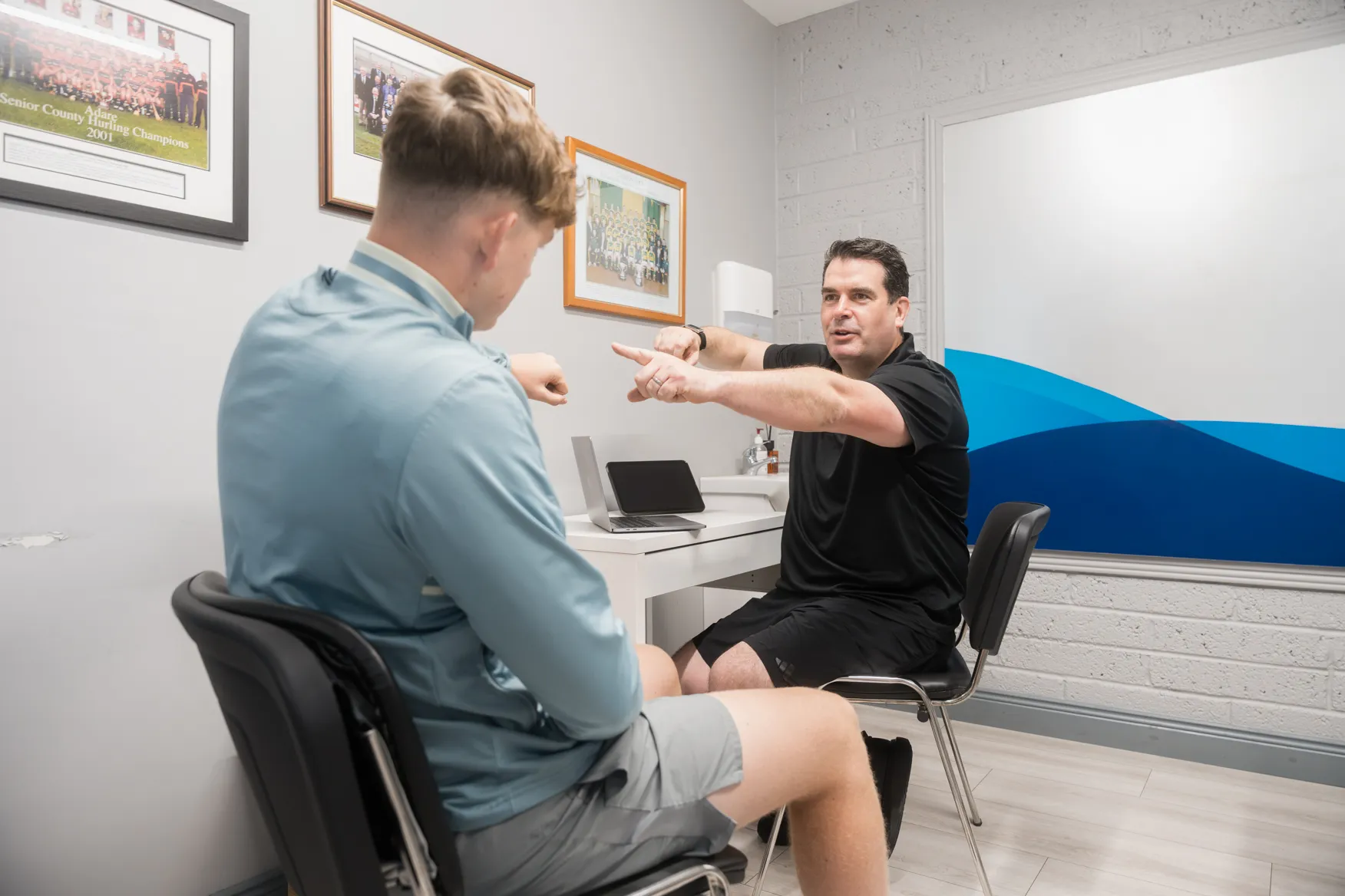 A physiotherapist demonstrating a movement to a young patient during a consultation